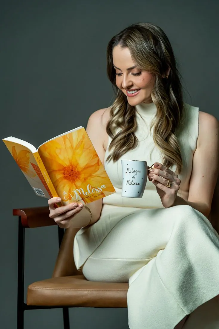 Ana lendo o livro com a caneca Milagre de Melissa